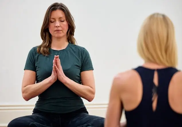 Two seated women, one has her hands clasped together doing yoga