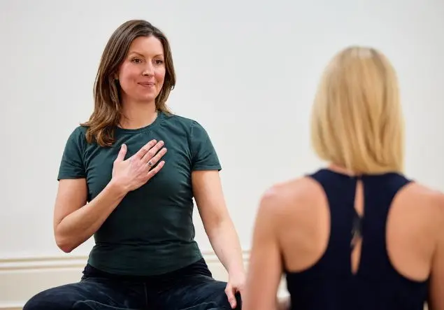 A woman places her hand on her heart while seated for yoga