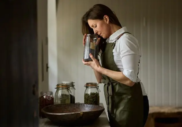 A woman smells a herbal mixture from a glass jar