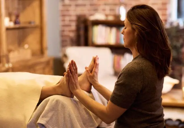 A woman performs Reiki, holding palms to feet