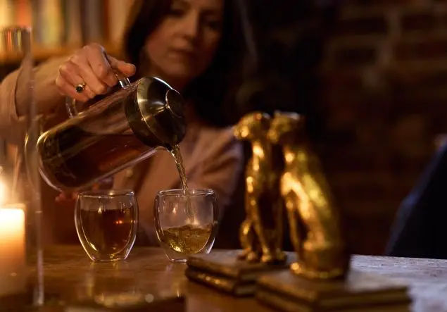 Tea is poured from a carafe into two glass mugs