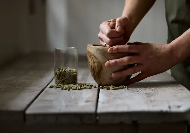 Hands using a wooden pestle and mortar crush up some cardamom pods