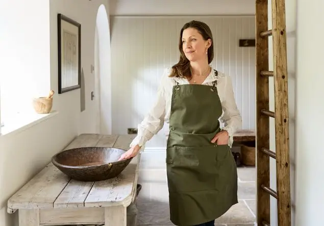 Kate Goodwin, wearing a green apron, places her hand on a large wooden bowl