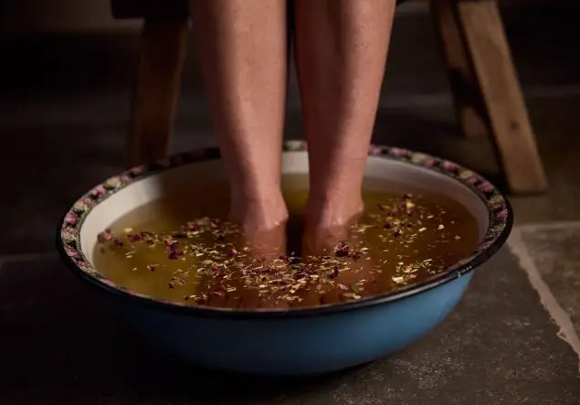 Feet soaking in a herbal foot bath in a decorative bowl