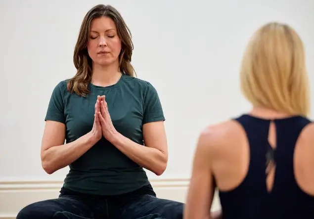 A woman doing yoga sits with her eyes closed and hands in the prayer position