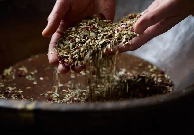 Hands lifting a mixture of herbs in a wooden bowl
