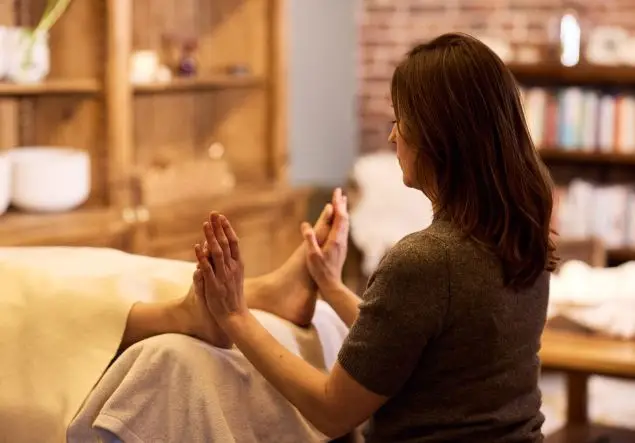 A woman performs Reiki, holding palms to feet