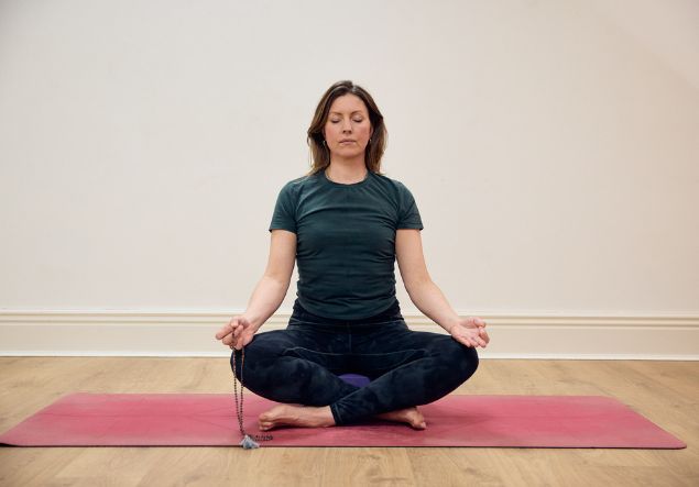 A seated woman meditates doing yoga with her eyes closed